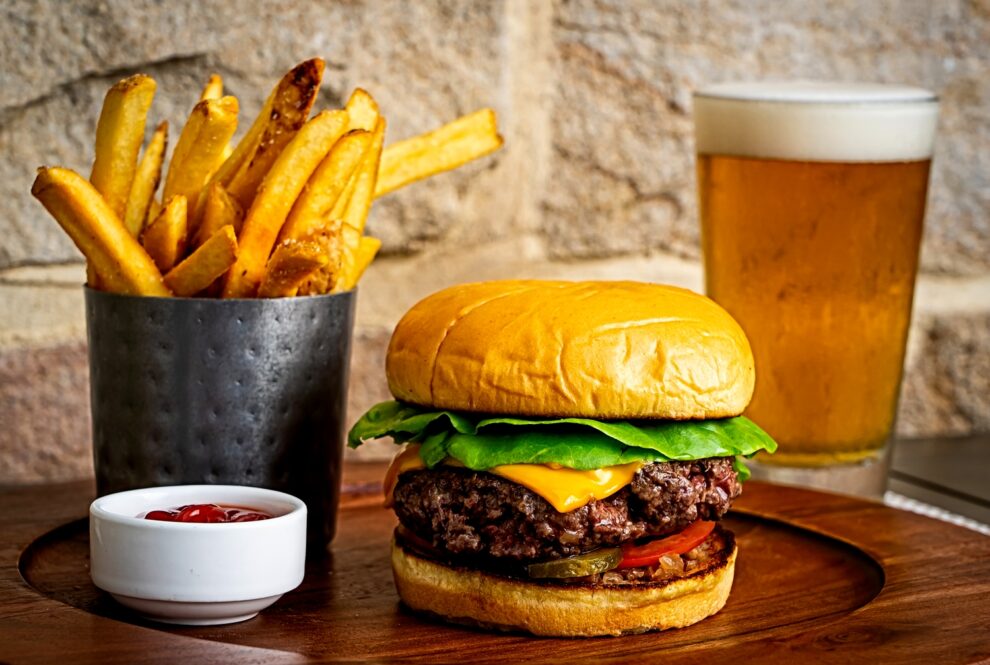 Burger on wooden platter with cup of french fries and glass of beer