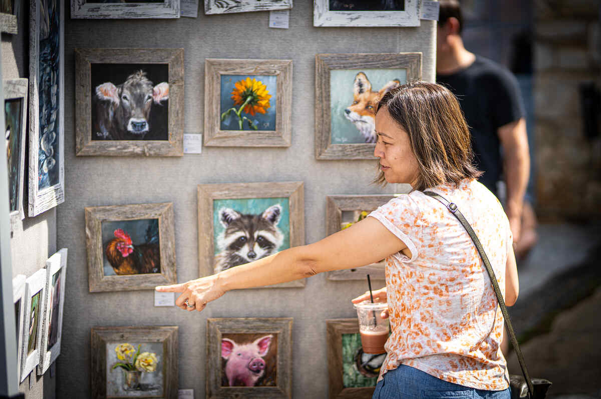 woman browsing animal and nature paintings pointing at a painting during art in the burg event