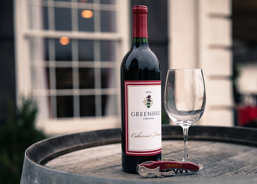 Bottle of Greenhill Cabernet Franc with wine glass and opener on a barrel
